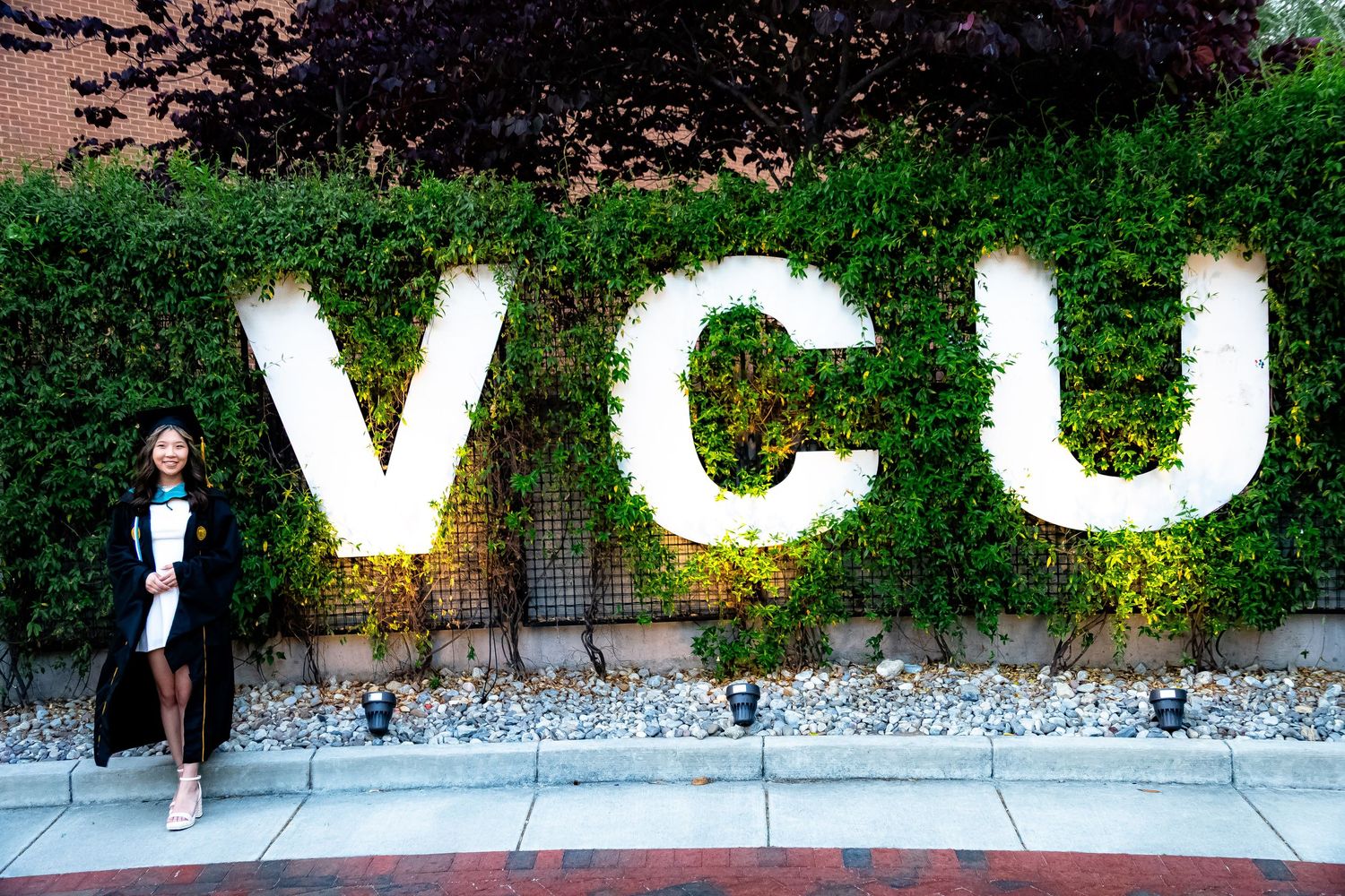 Large white VCU letters mounted on green hedge wall.