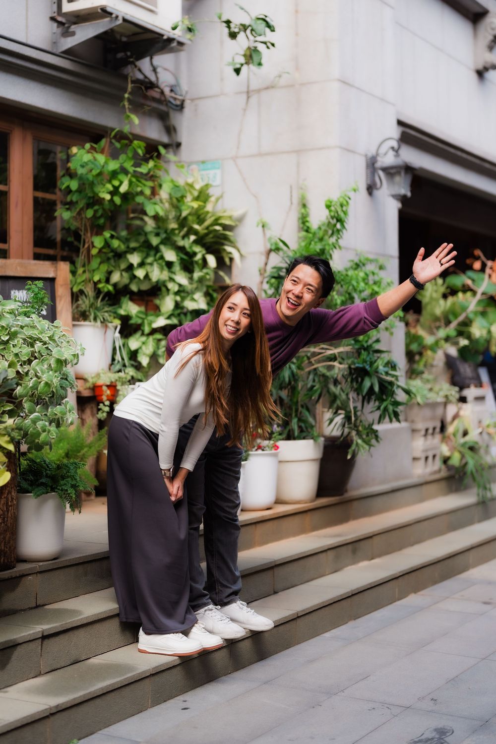 A couple joyfully waves on the steps surrounded by potted plants and greenery at Dihua Street in Dadaocheng, Datong District, Taipei.