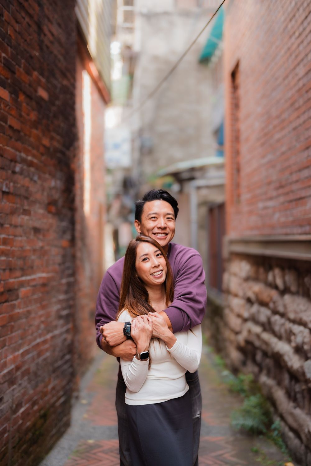 A couple hugs in a narrow brick alleyway with warm lighting at Dihua Street in Dadaocheng, Datong District, Taipei.