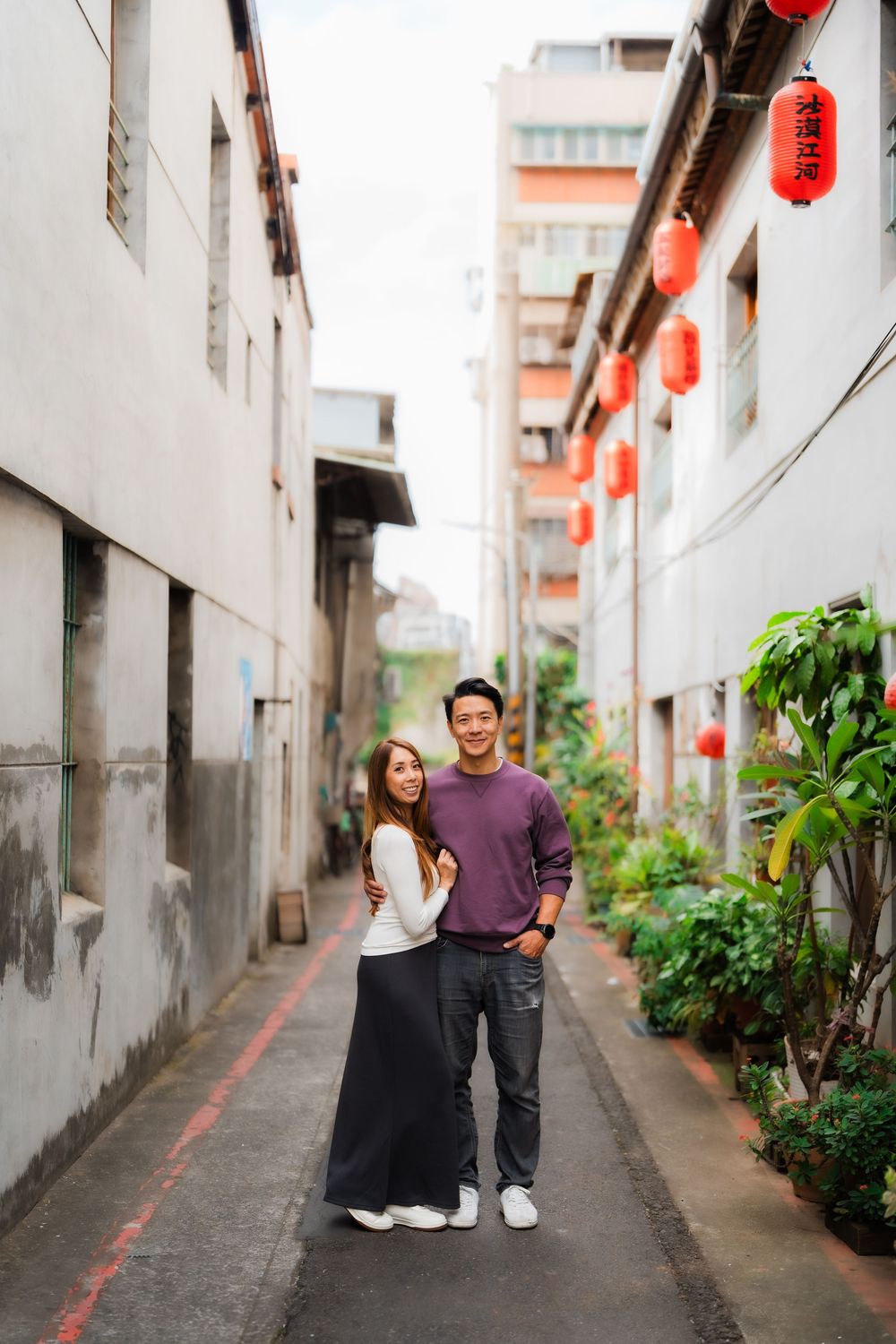 A couple standing in a narrow alley with red lanterns and greenery at Dihua Street in Dadaocheng, Datong District, Taipei.