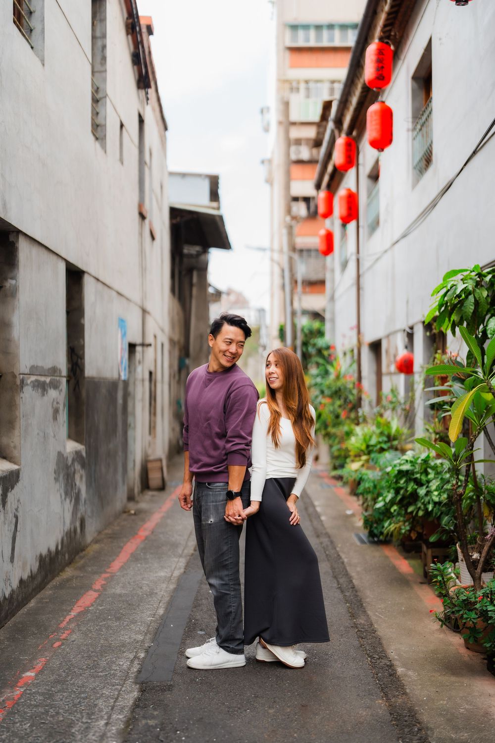 A couple stands back-to-back in a narrow alley decorated with red lanterns in Dadaocheng.