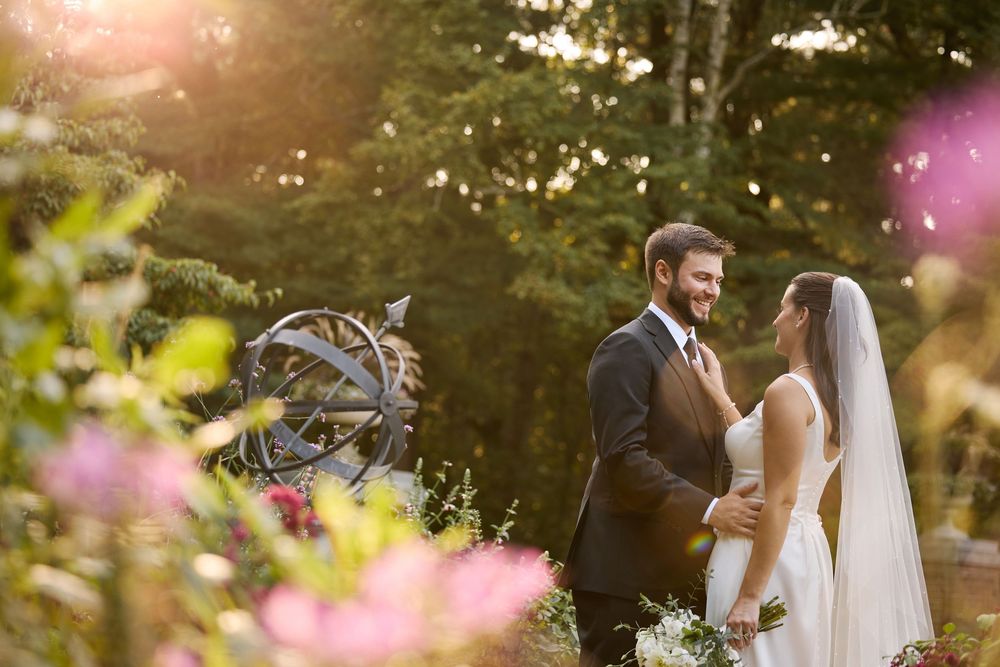 Bride and groom share a romantic moment in a sunlit garden with blooming flowers and lush greenery at golden hour.