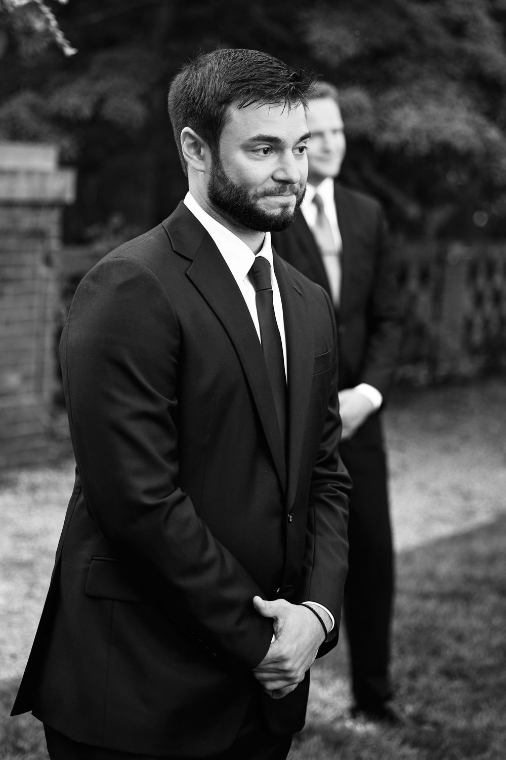 Black and white photo of a bearded man in a dark suit and tie standing outdoors at a formal event.