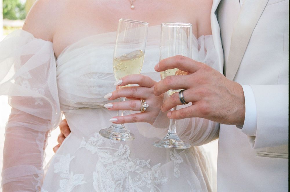 Bride and groom toasting with champagne glasses, bride wearing white lace wedding dress with diamond ring.