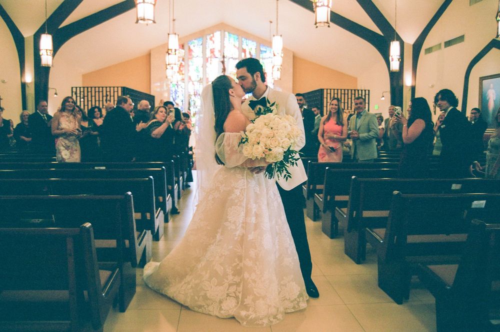 Bride and groom share a kiss at the church altar after their wedding ceremony, surrounded by guests in pews.