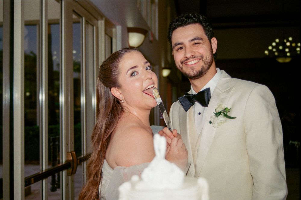 Bride and groom smiling while cutting their white wedding cake at a elegant evening reception.