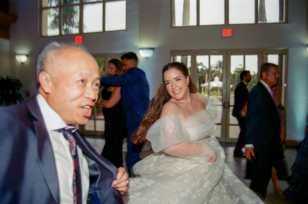 Bride in elegant white gown smiles with older gentleman at wedding reception dance floor.