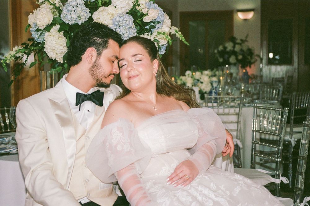Bride and groom share a tender moment at wedding reception, surrounded by elegant floral arrangements.