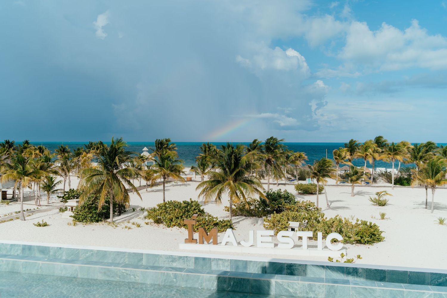 Beach wedding venue at Majestic Elegance Costa Mujeres with a Caribbean rainbow and stormy sky in the background.