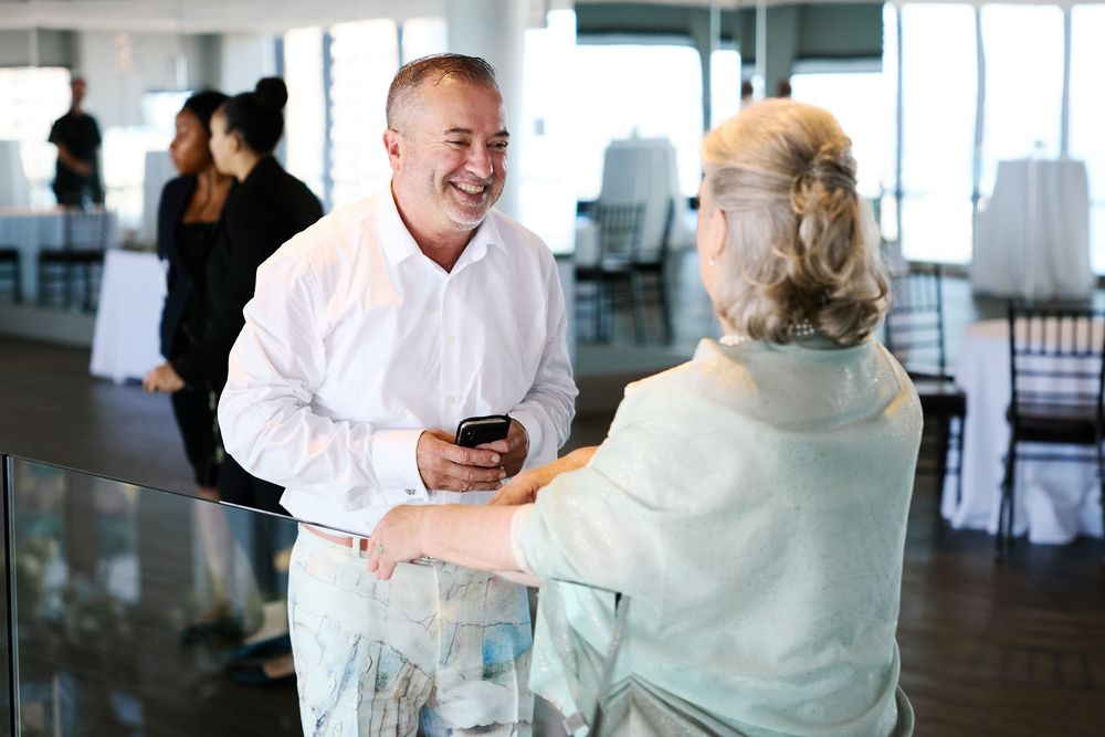 Smiling man in white shirt converses with seated woman at elegant wedding venue reception.