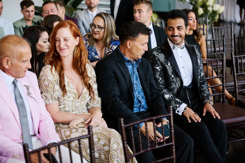 Guests smile and laugh while seated at an elegant outdoor wedding ceremony.
