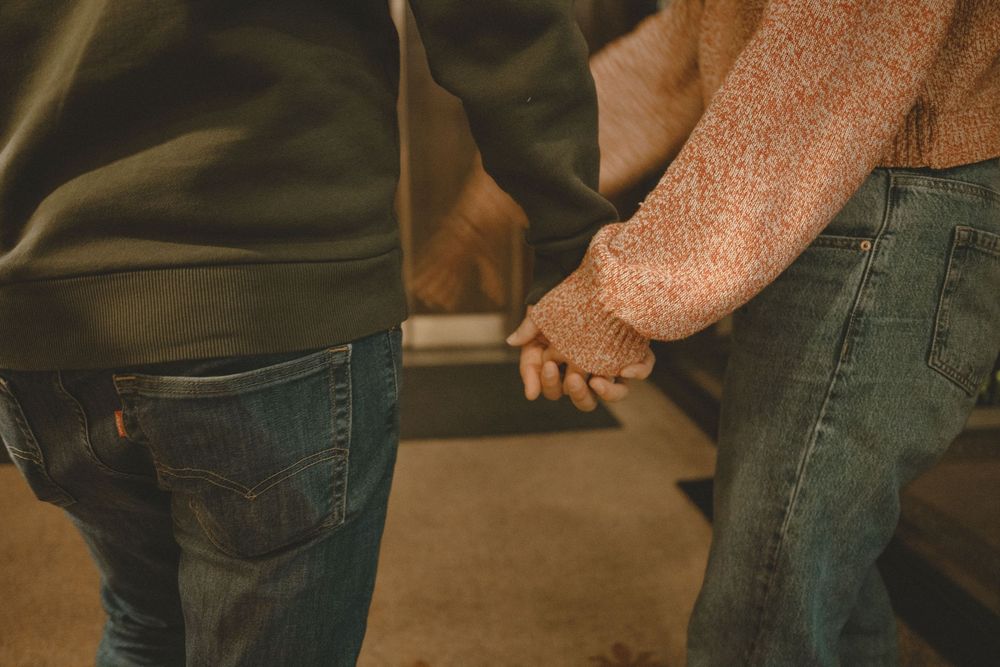 Two people holding hands while standing close together, wearing casual jeans and sweaters.