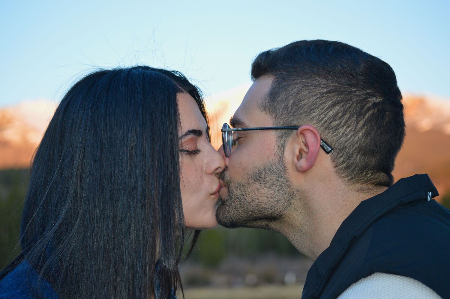 Man and woman kissing after he proposed to her at Sprague Lake. Alpenglow lit mountains in the background.