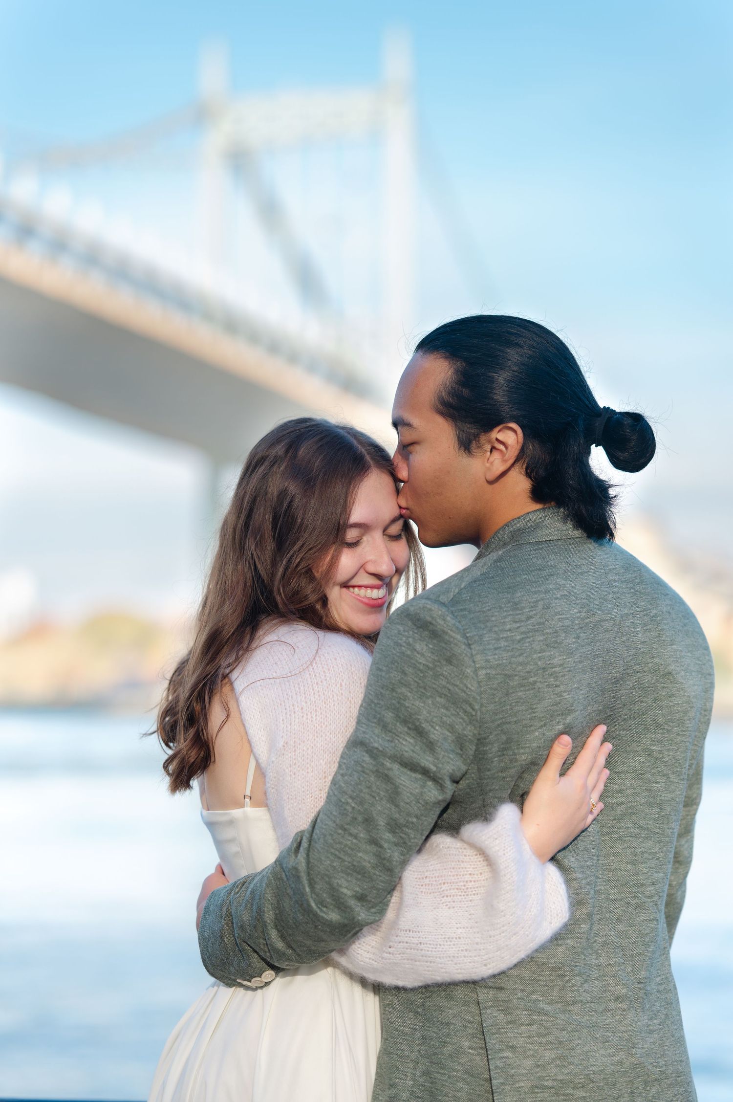 Couple sharing a romantic kiss under a grand stone bridge arch with repeating archways and green grass in Queens, NYC.