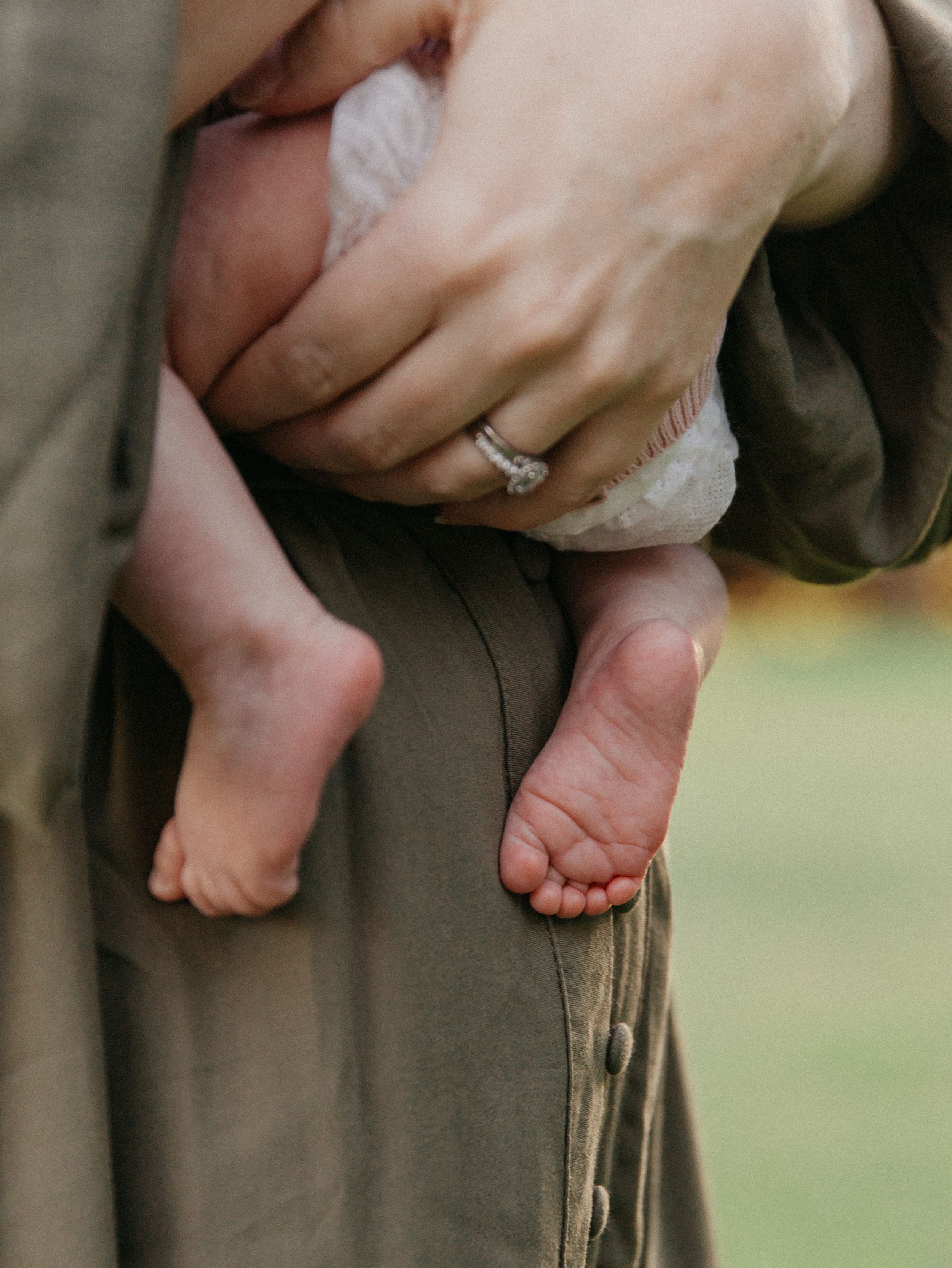 Close-up of a parent holding a newborn baby, showing tiny feet and a diamond engagement ring.