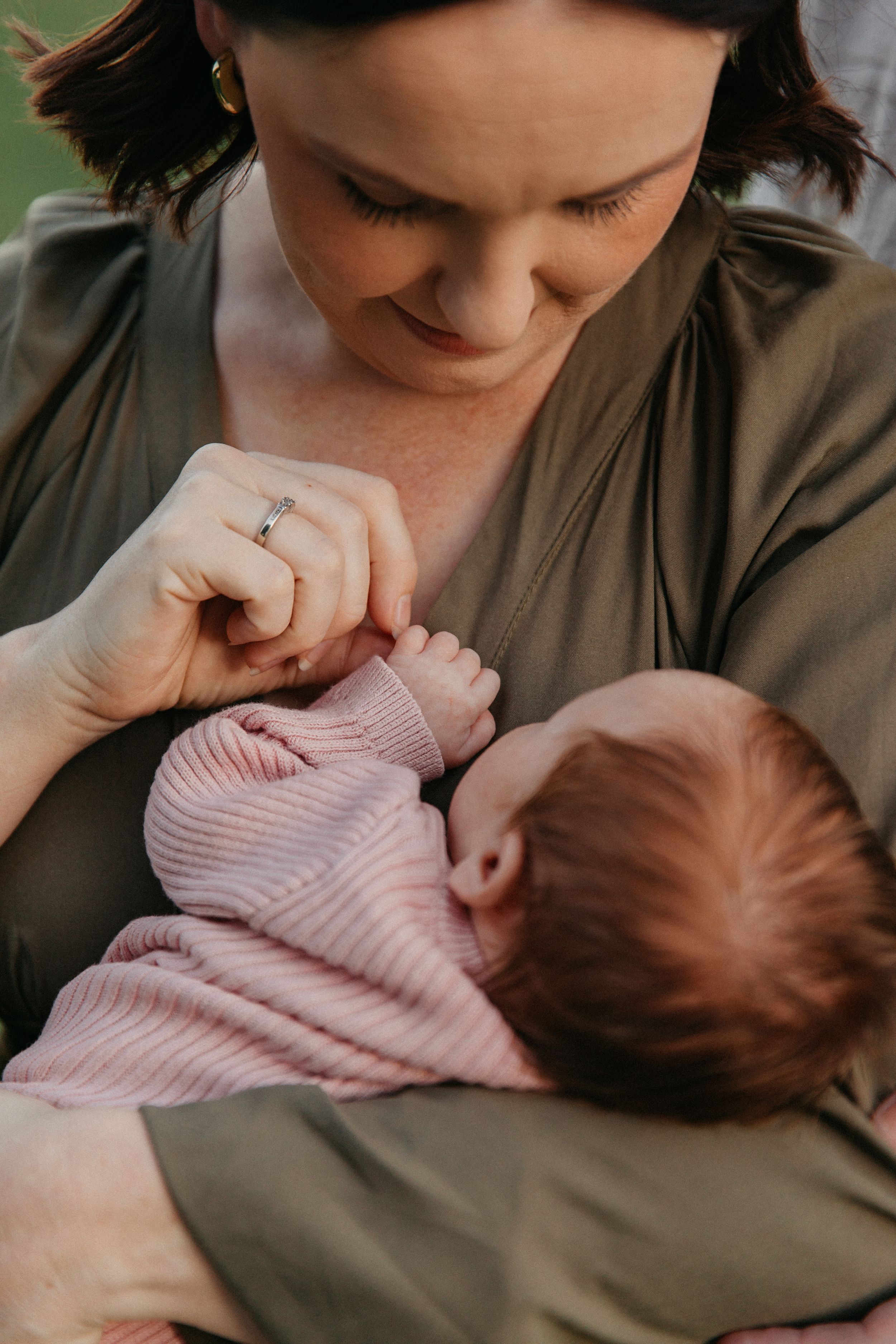 Mother tenderly holding newborn baby in pink outfit, sharing a gentle moment outdoors.