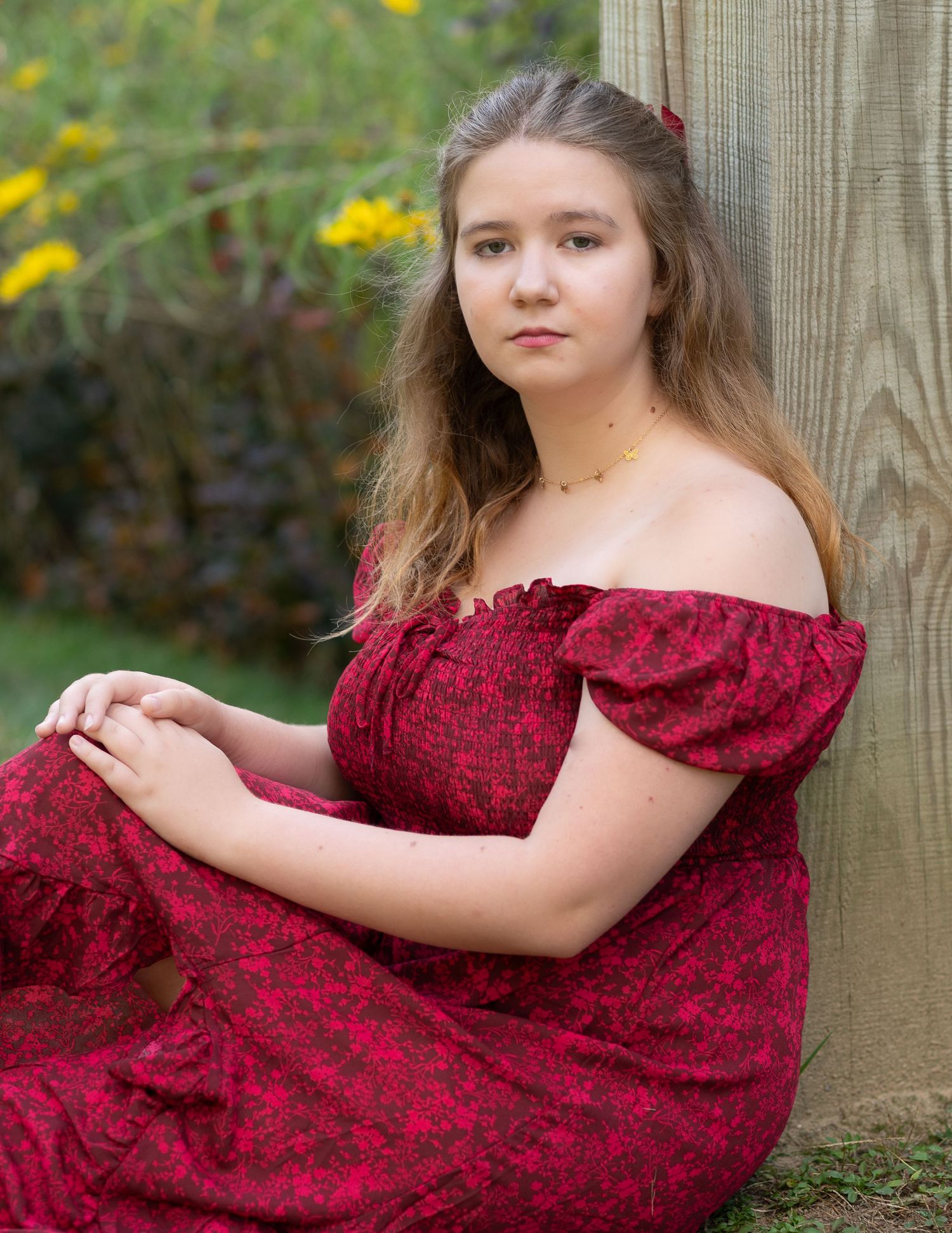 Young woman in red off-shoulder dress standing gracefully in tall golden grass field during golden hour.