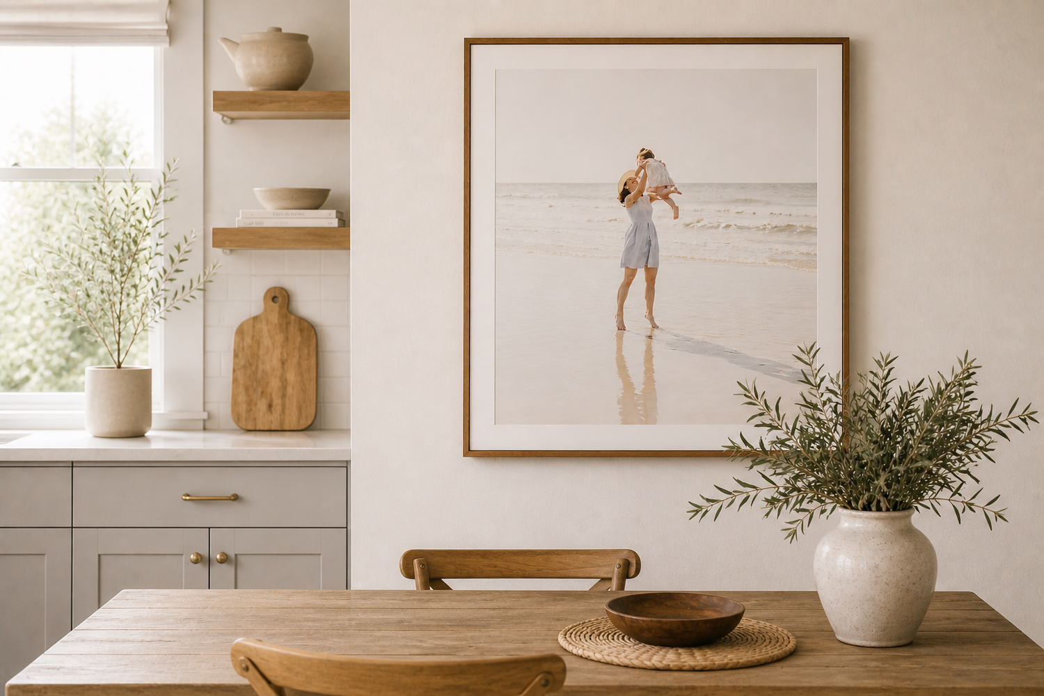 Coastal framed photo print of a mom in sunhat with child on the beach displayed in a bright, modern dining room with wood table and shelves.