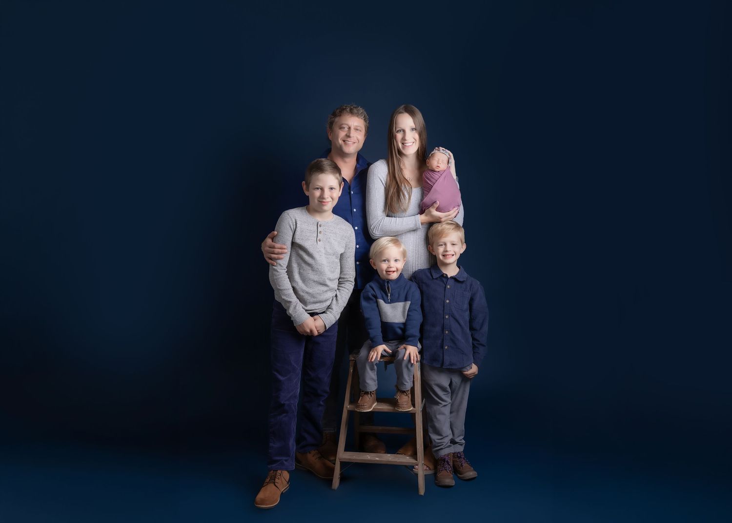 Family of six posing together against a dark navy blue background in a professional studio portrait photo.