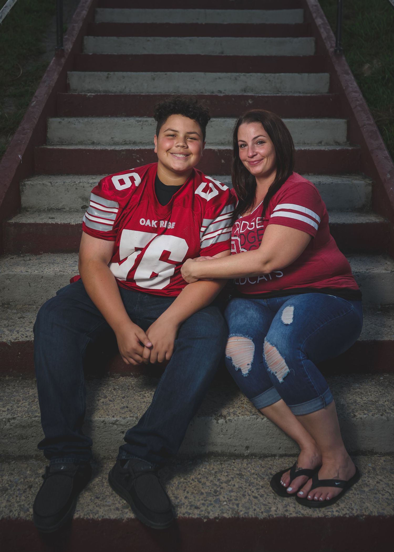 Two people in red football jerseys sitting on brick steps, smiling together in a warm portrait photo.