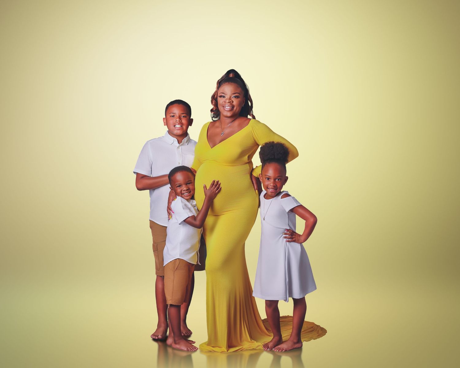 Pregnant woman in yellow gown poses with three children in a professional maternity photo shoot.