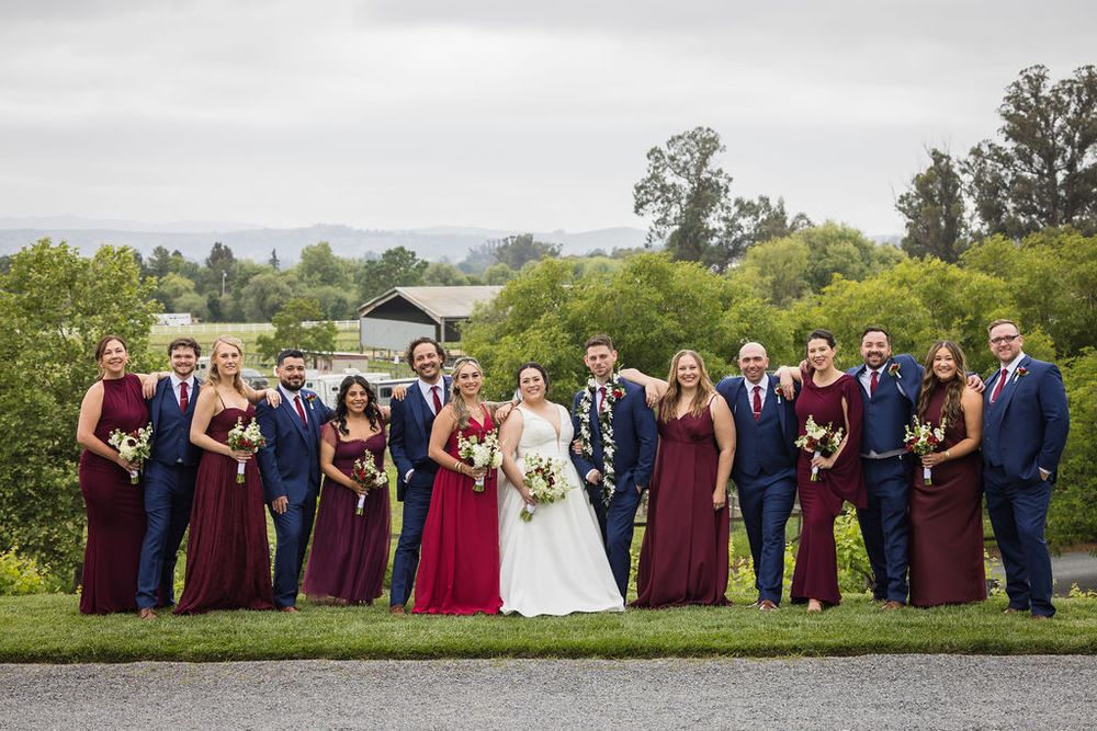 Wedding party in burgundy and navy attire posing outdoors at a lush garden venue.