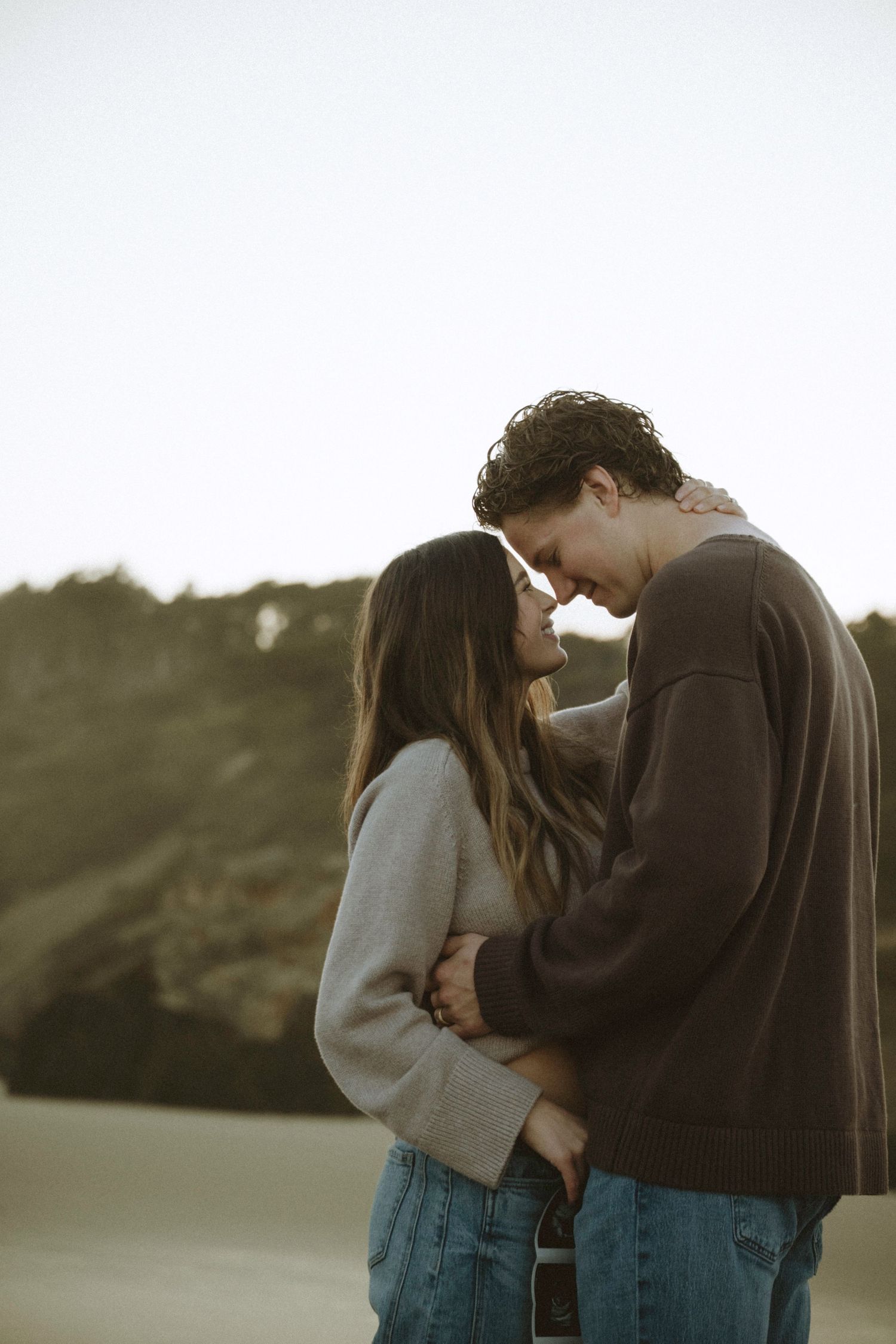 A romantic couple shares an intimate moment on a beach, touching foreheads tenderly in soft golden light.