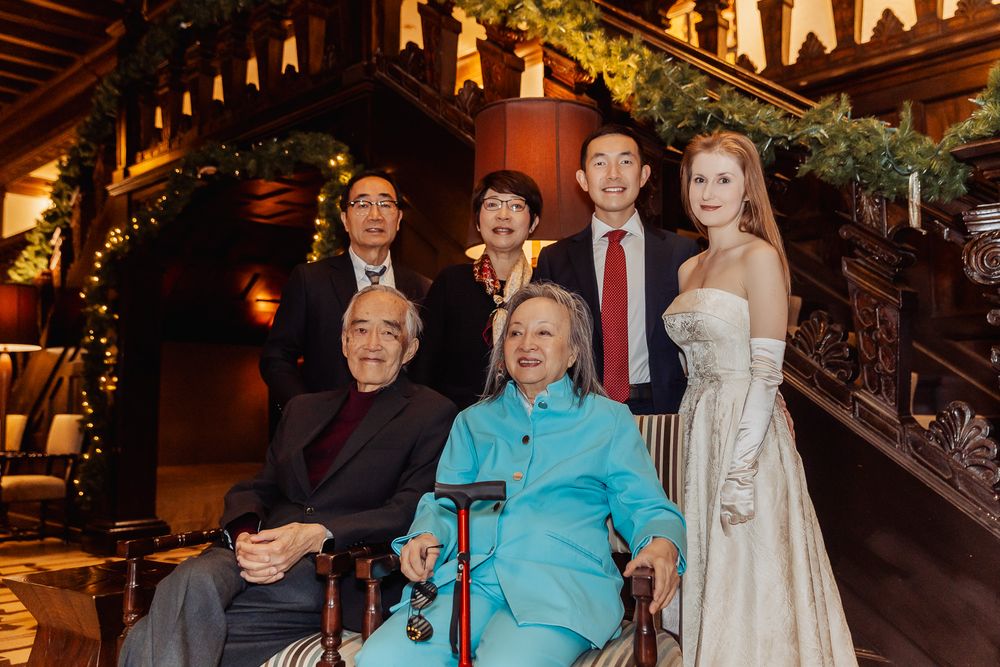 Group of seven people posing for a formal photo on a decorated staircase at an elegant holiday event.