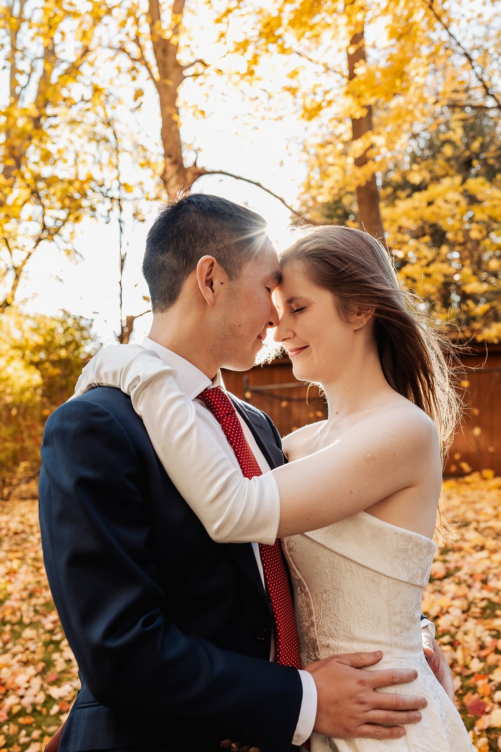 A bride and groom share a romantic moment in an autumn park, surrounded by golden fall foliage.