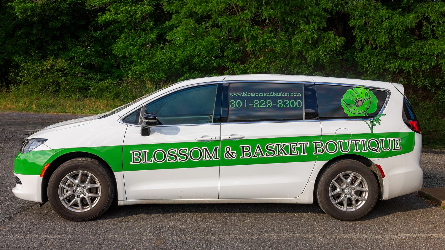 White Blossom & Basket Boutique delivery van with green logo wrap parked in lot, florist shop vehicle.