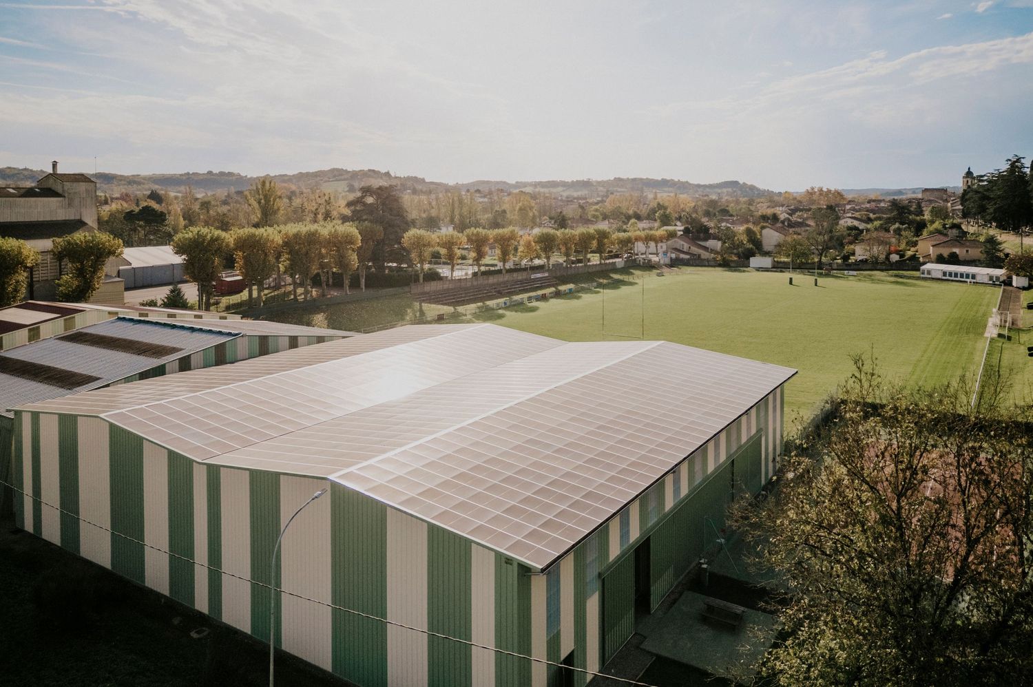Reportage photo industriel en drone. Ombrières photovoltaïques intégrées à un site sportif dans le Gers, avec terrain de tennis et paysage.