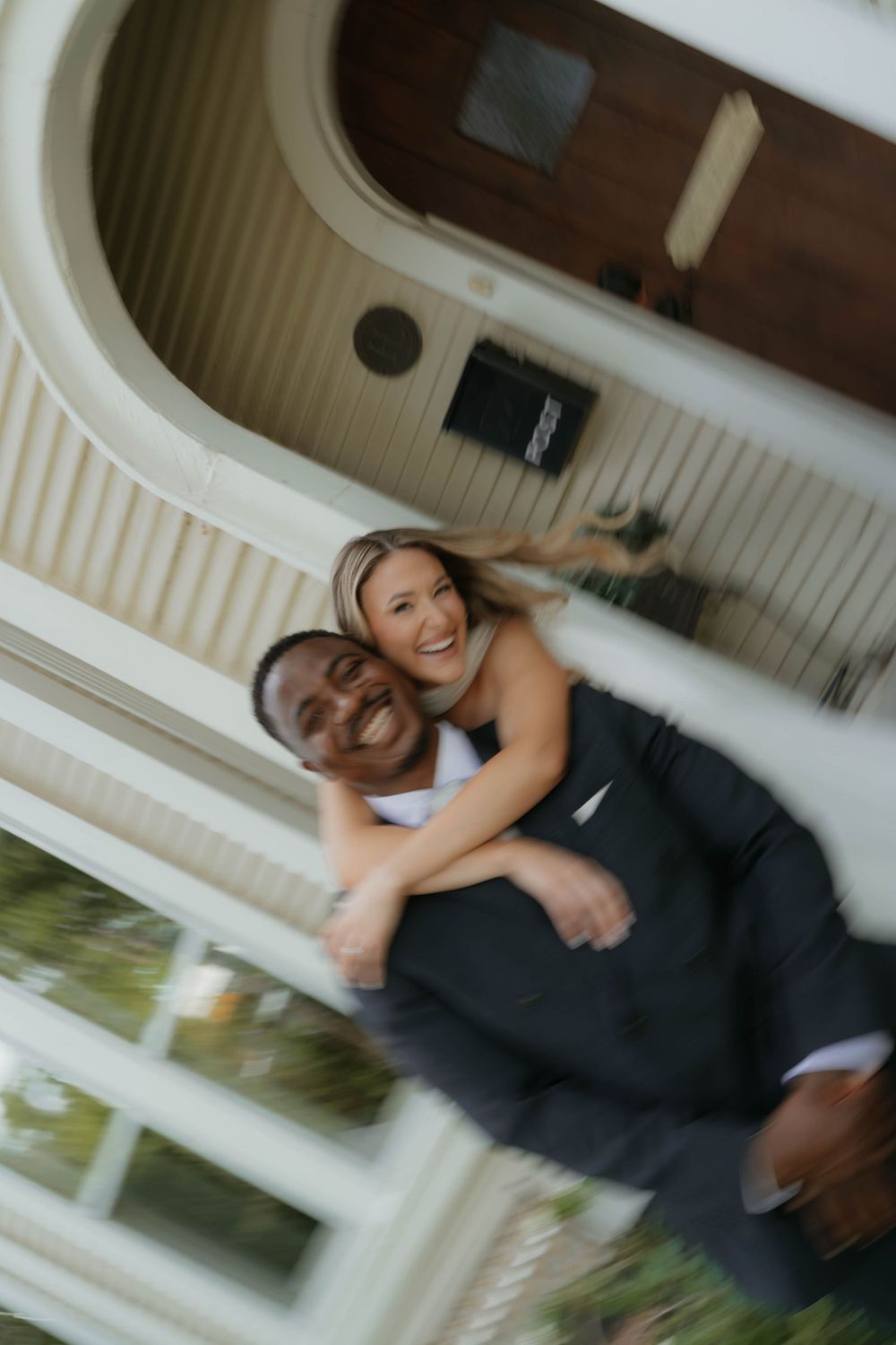 Creative upside-down photo of laughing bride and groom outside cream-colored building with arched porch.