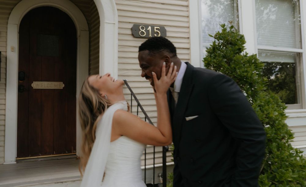 Bride and groom share a kiss outside cream building numbered 815 surrounded by green shrubs.