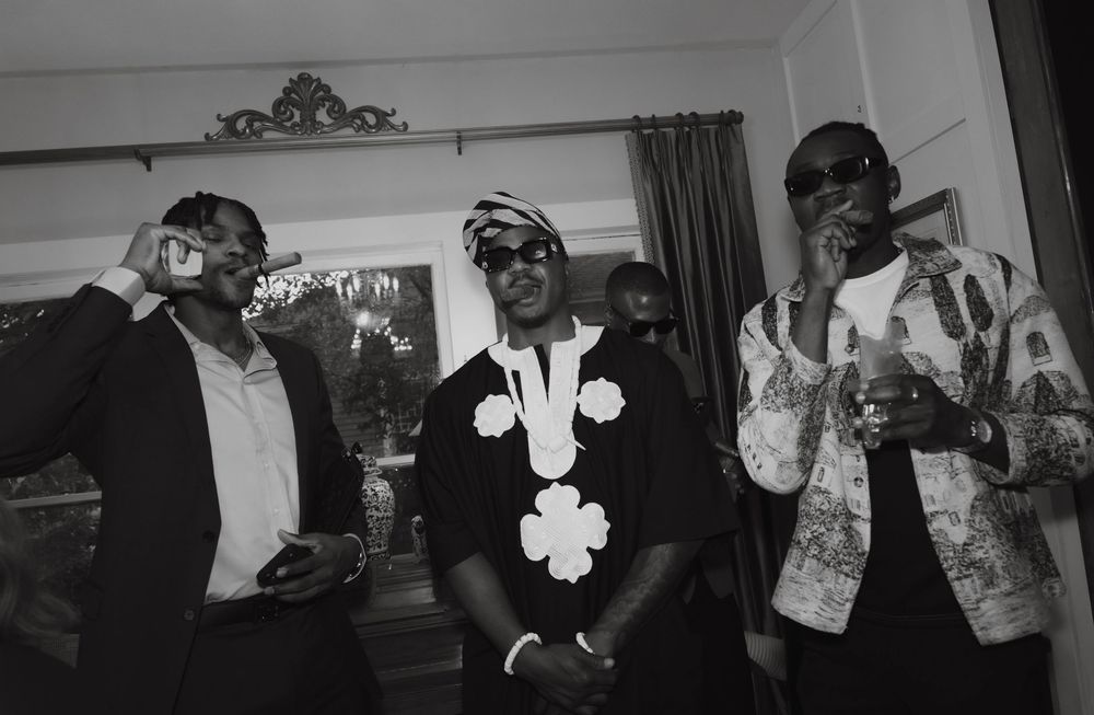 Three men pose indoors in stylish outfits, captured in black and white photography.