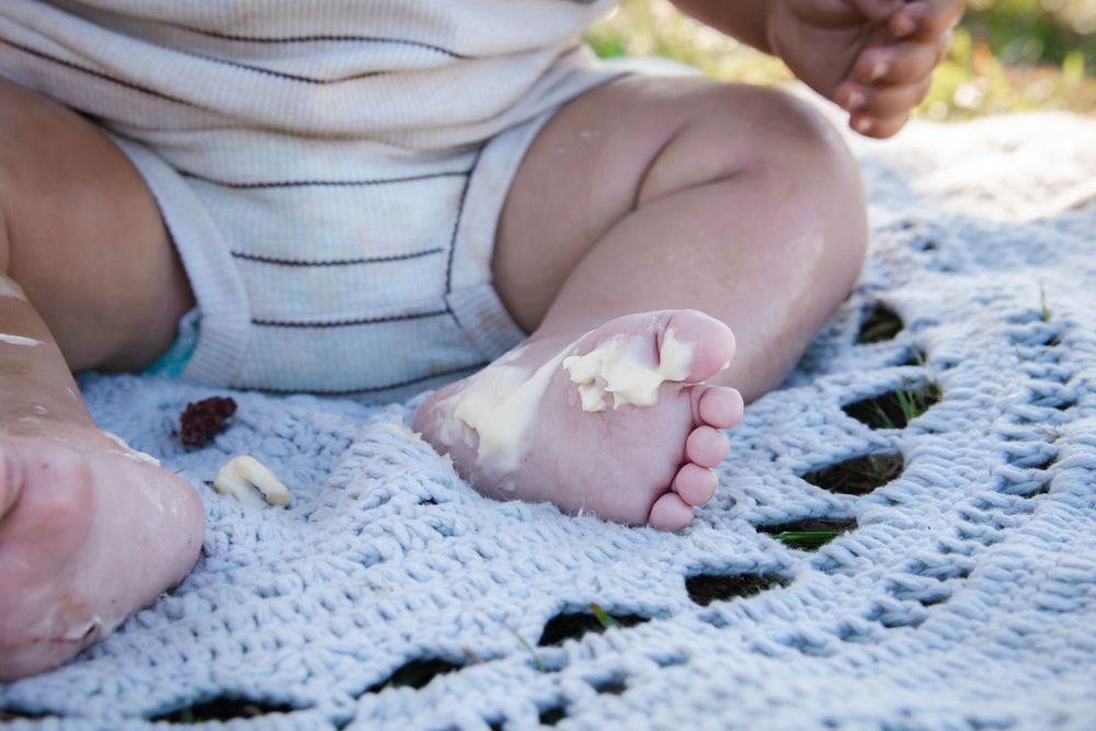 Small baby feet resting on a white crocheted blanket outdoors in natural sunlight.