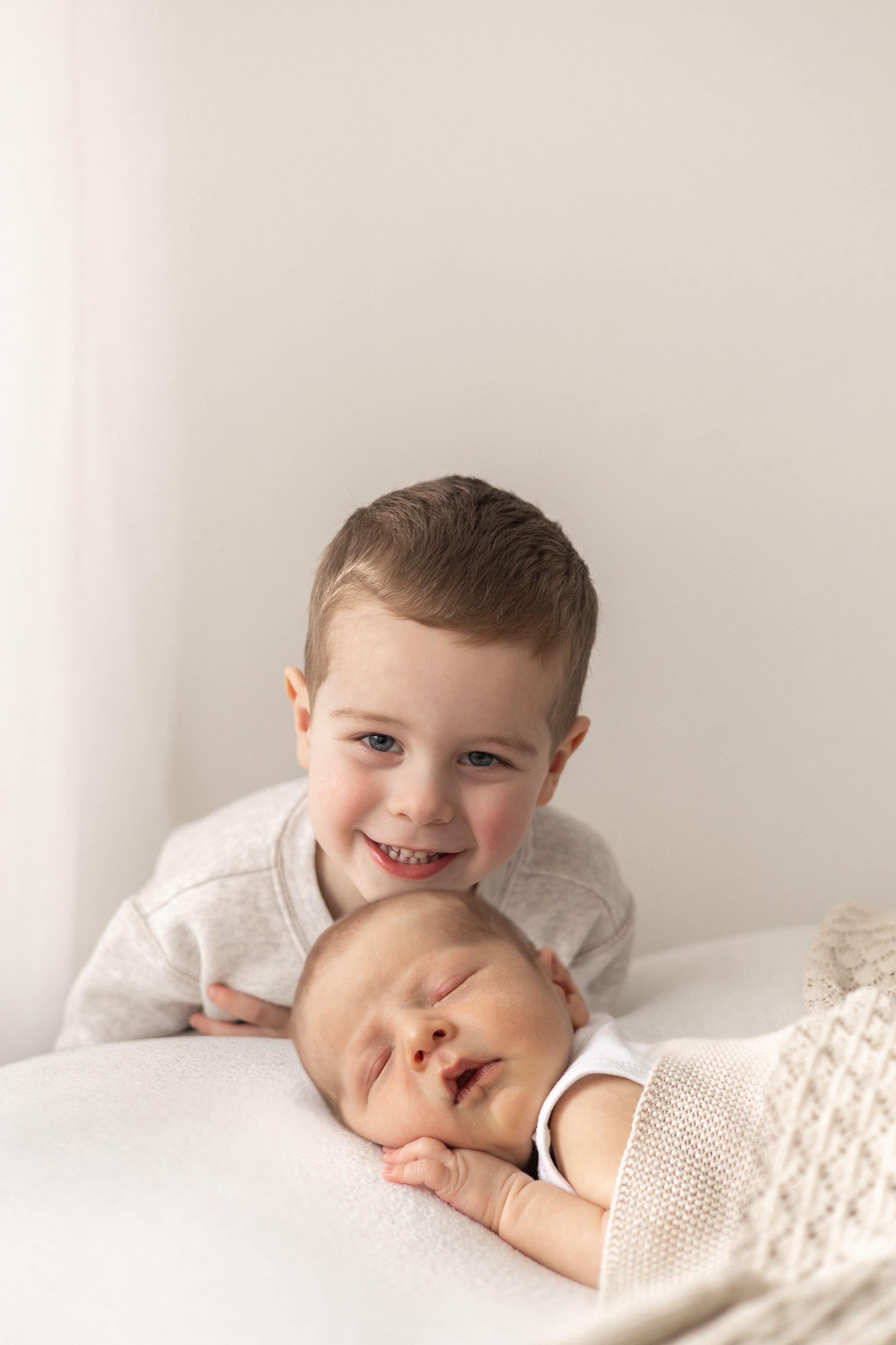 Smiling boy posing with sleeping newborn baby sibling in soft white natural studio Nottingham newborn photographer