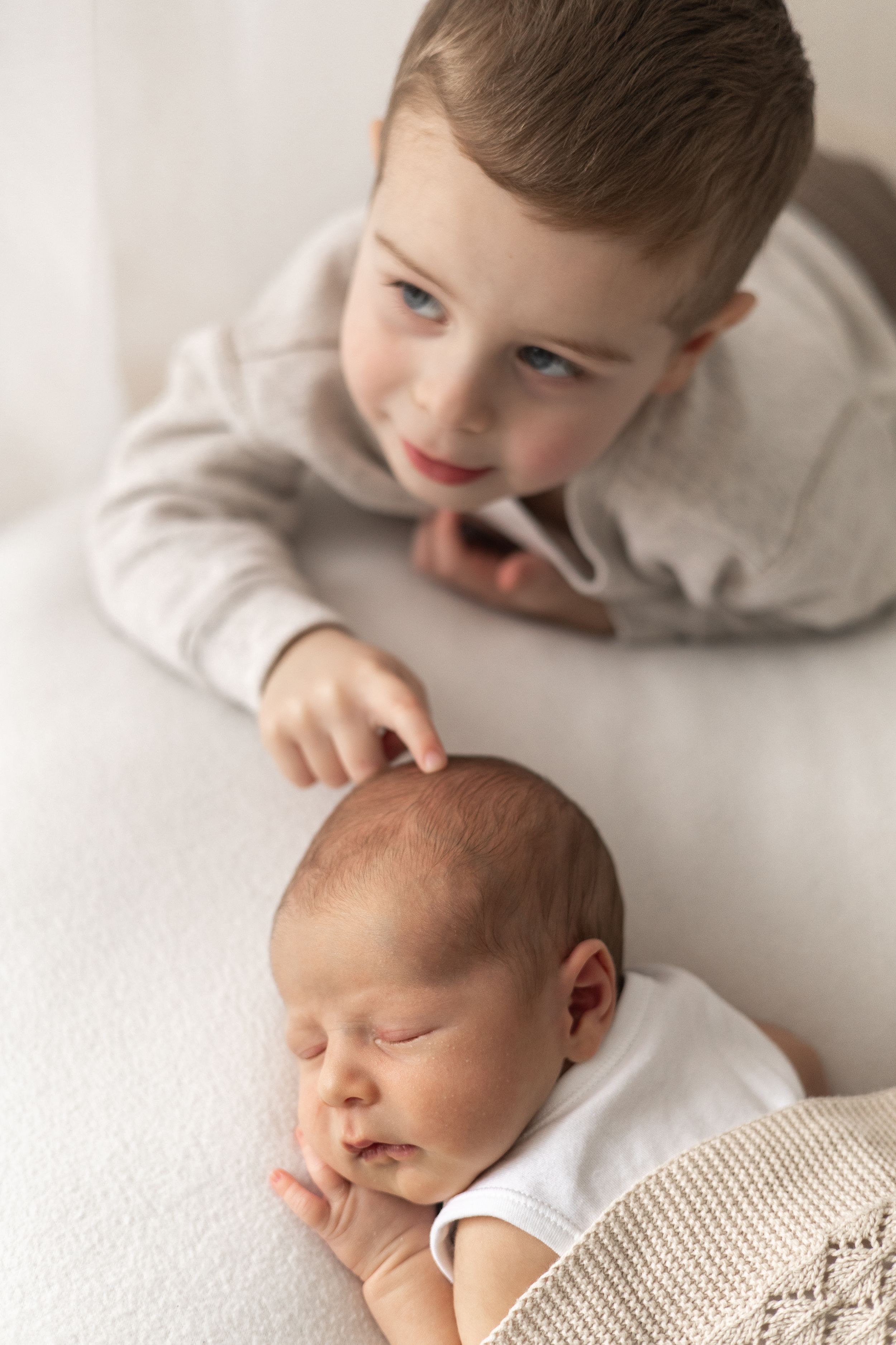 Young sibling boy with blue eyes gently touching sleeping newborn baby sibling during natural newborn photoshoot Nottingham