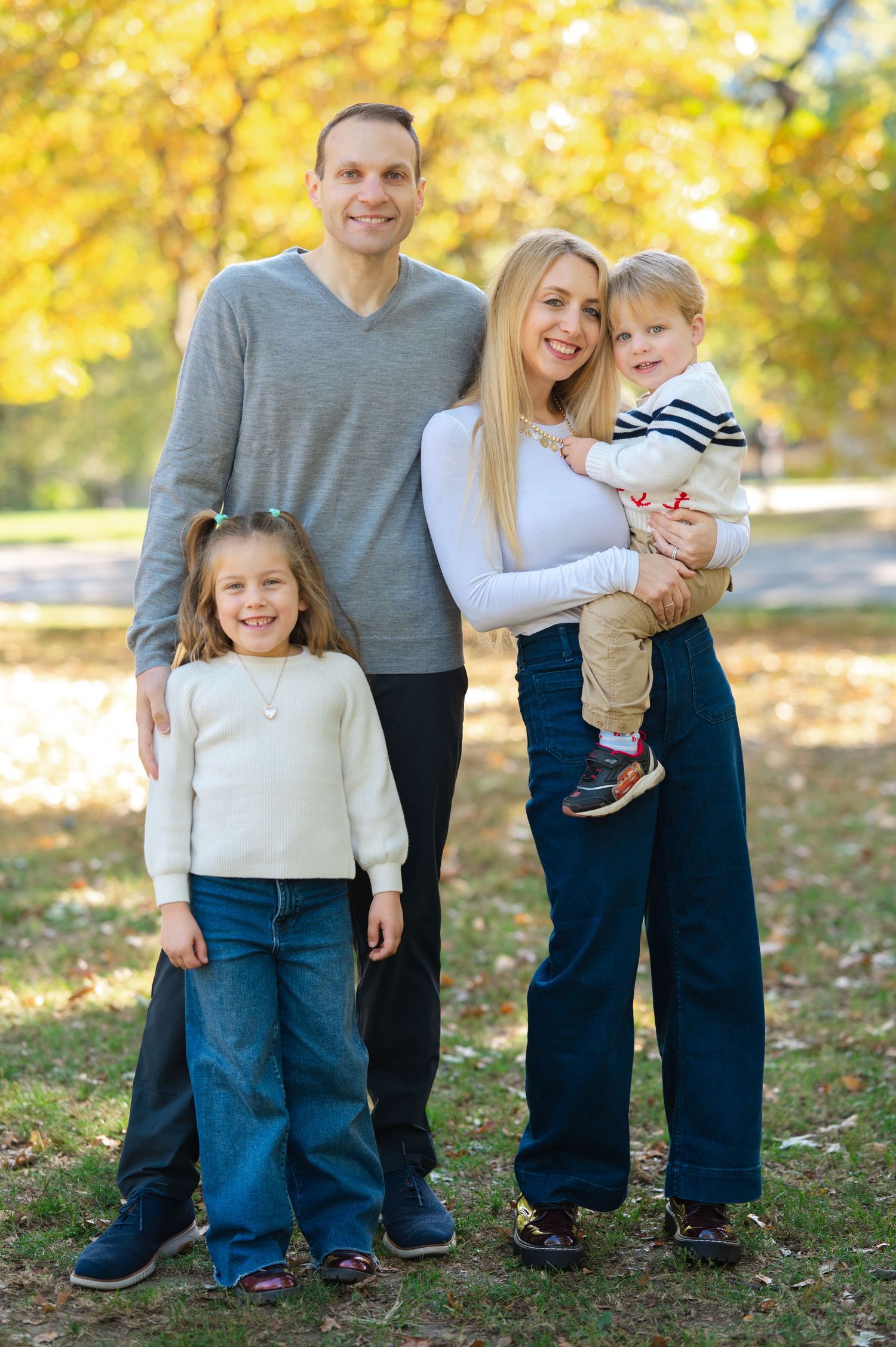 Happy family of four posing outdoors in autumn park with colorful yellow foliage in background in Central Park during a family photo session