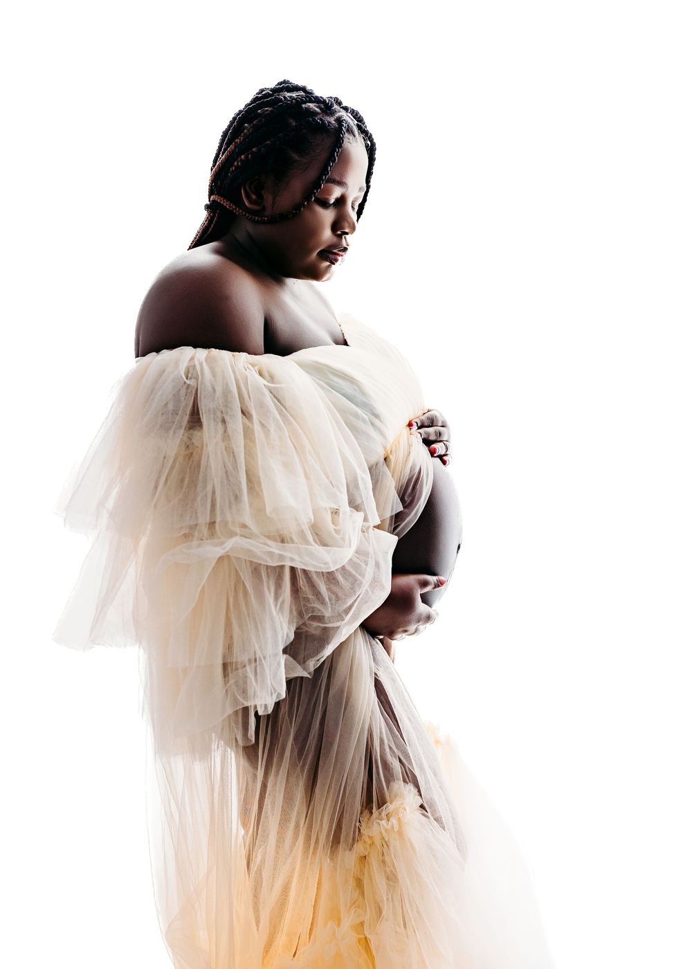 Pregnant woman in sheer yellow tulle robe cradling baby bump during elegant maternity photo session.