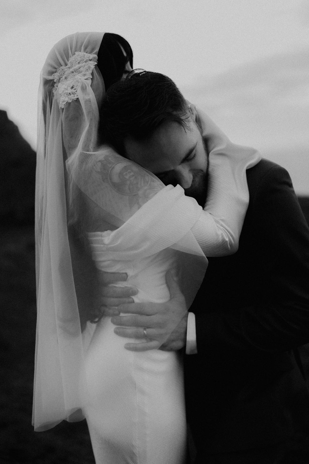 Black and white photo of bride and groom embracing tenderly, bride in veil and white gown, groom in suit.