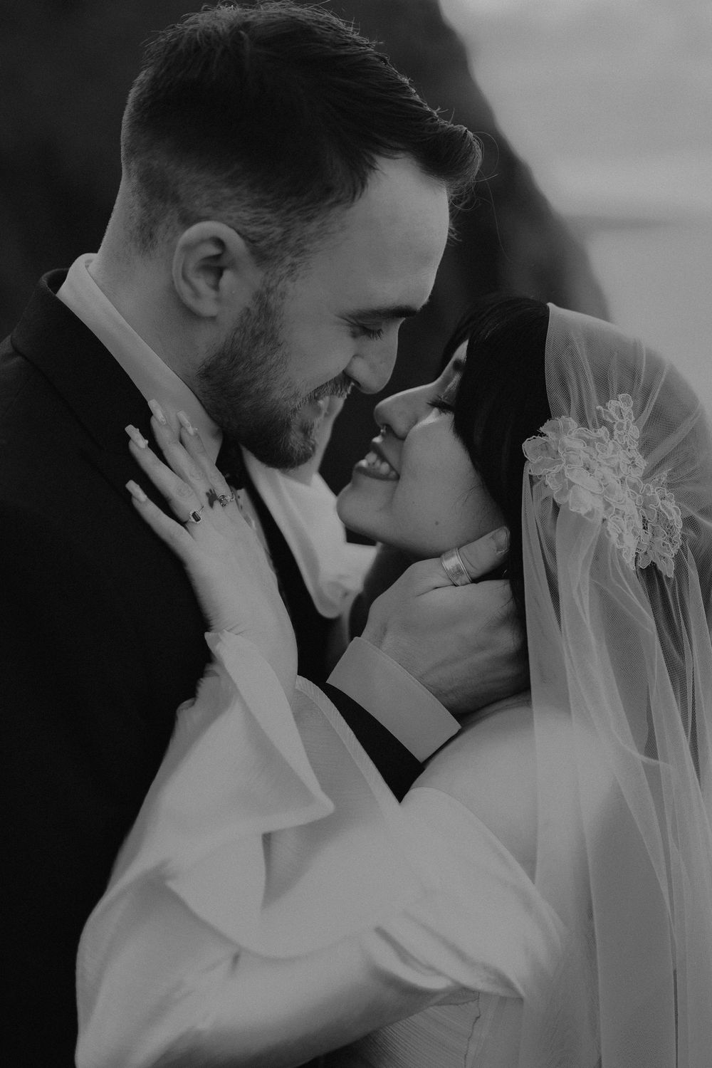 Black and white photo of a bride and groom sharing an intimate moment, smiling at each other during their wedding.