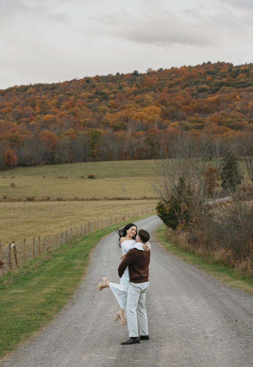 Couple sharing a romantic kiss beside a classic blue car surrounded by lush green trees outdoors.
