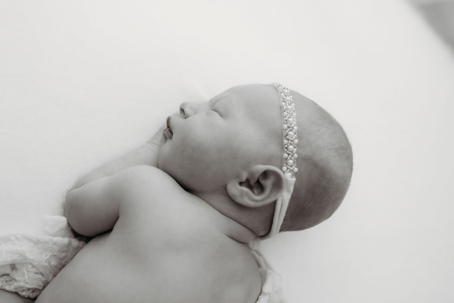 Black and white newborn baby girl sleeping peacefully wearing a delicate rhinestone headband.