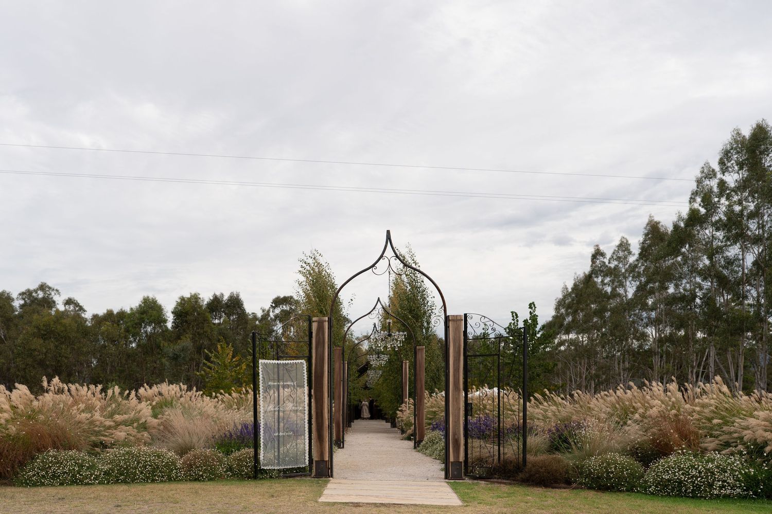 Ornate metal archway entrance to a garden path surrounded by ornamental grasses and eucalyptus trees.