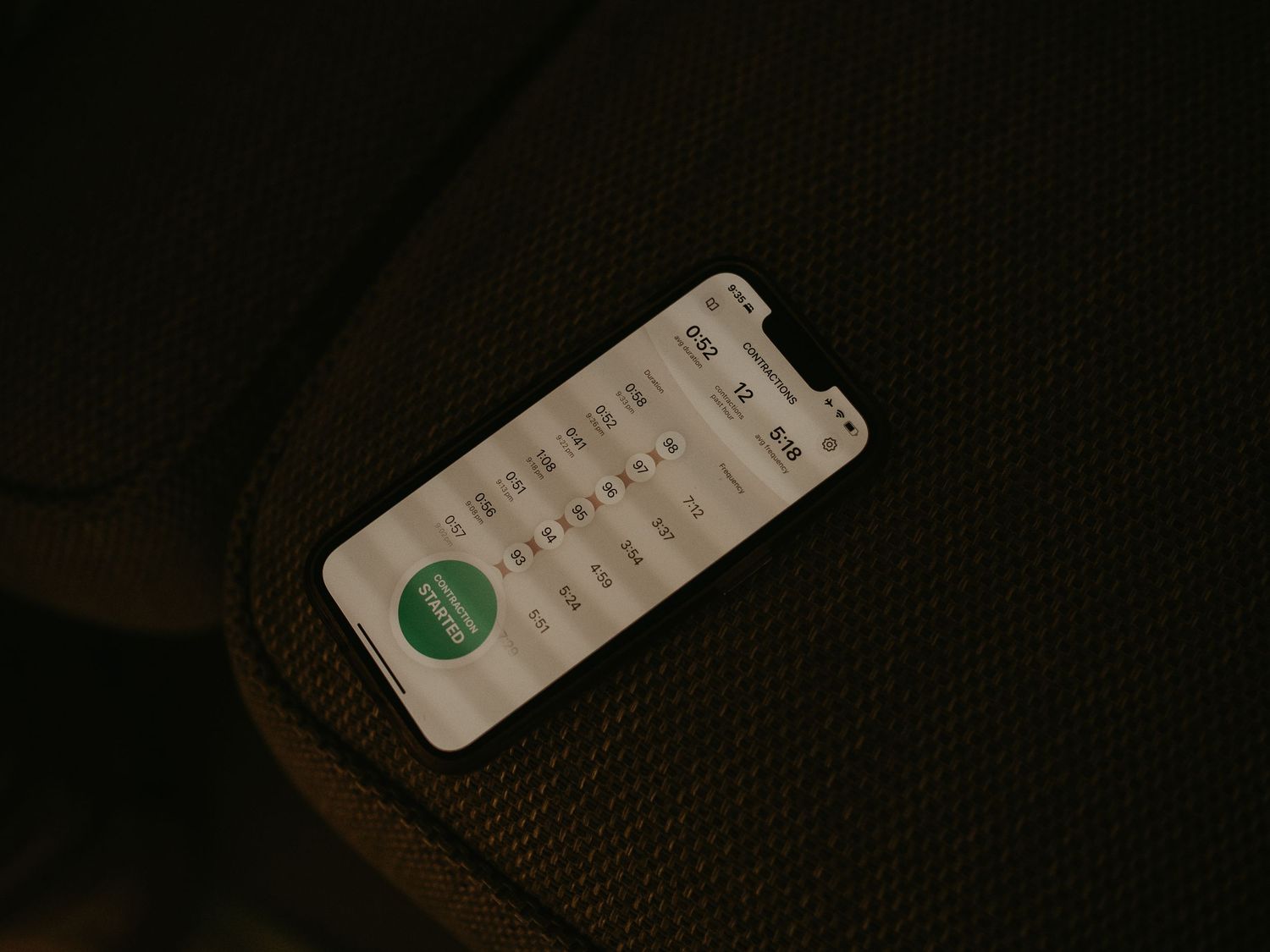 Smartphone displaying a messaging app with green icon resting on dark olive green backpack in dim lighting.