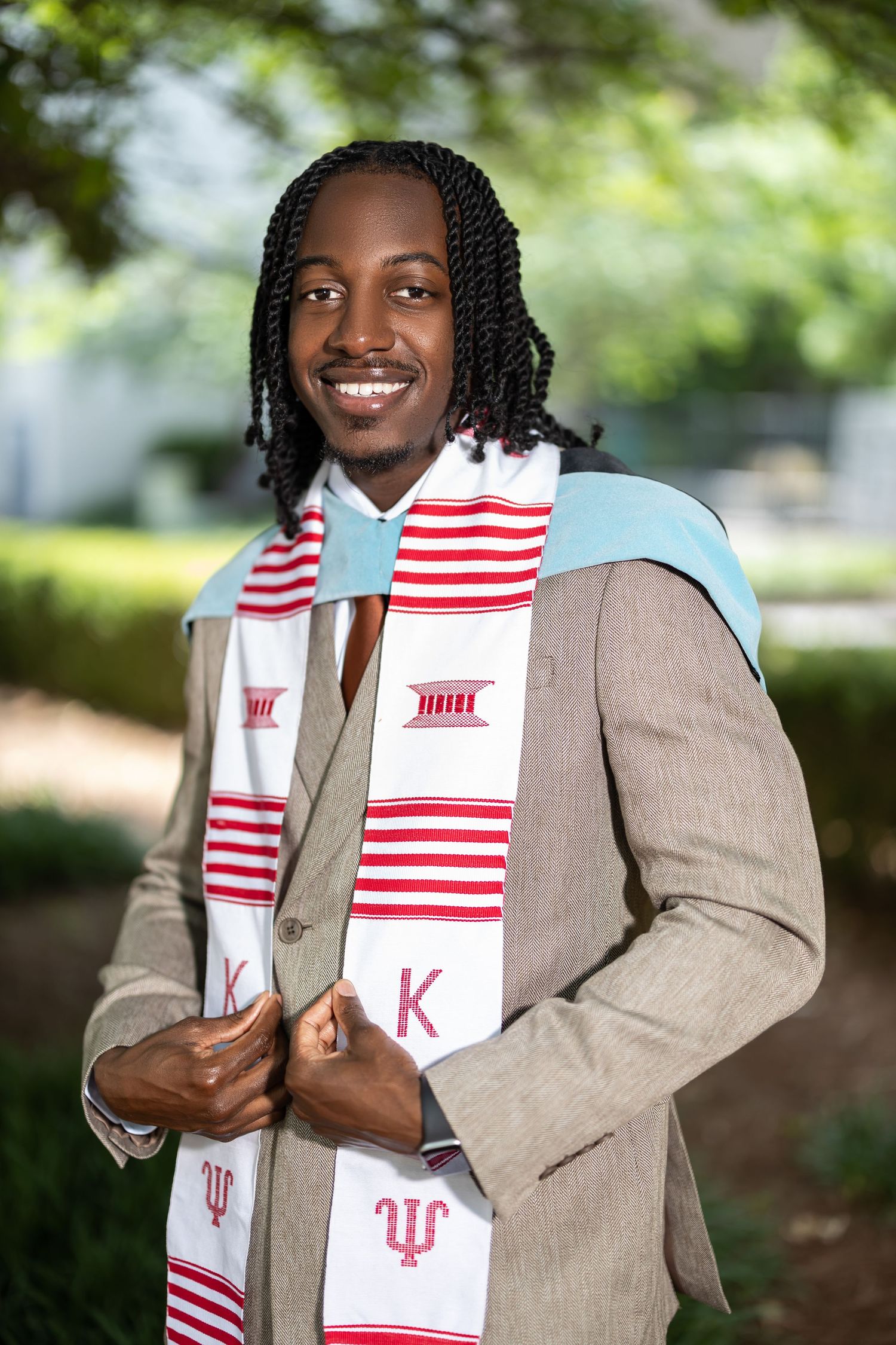 Smiling Black male graduate poses in tan suit with red and white Indiana University graduation stole.