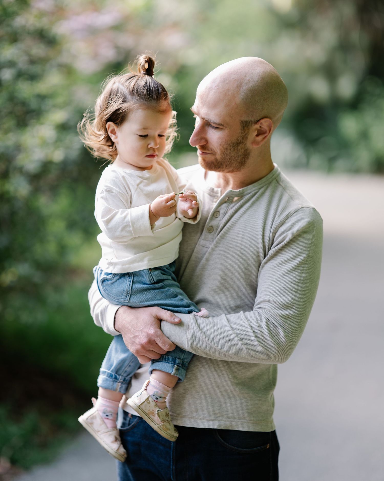 Black and white photo of a bald bearded man lovingly holding a toddler girl with a bun hairstyle.