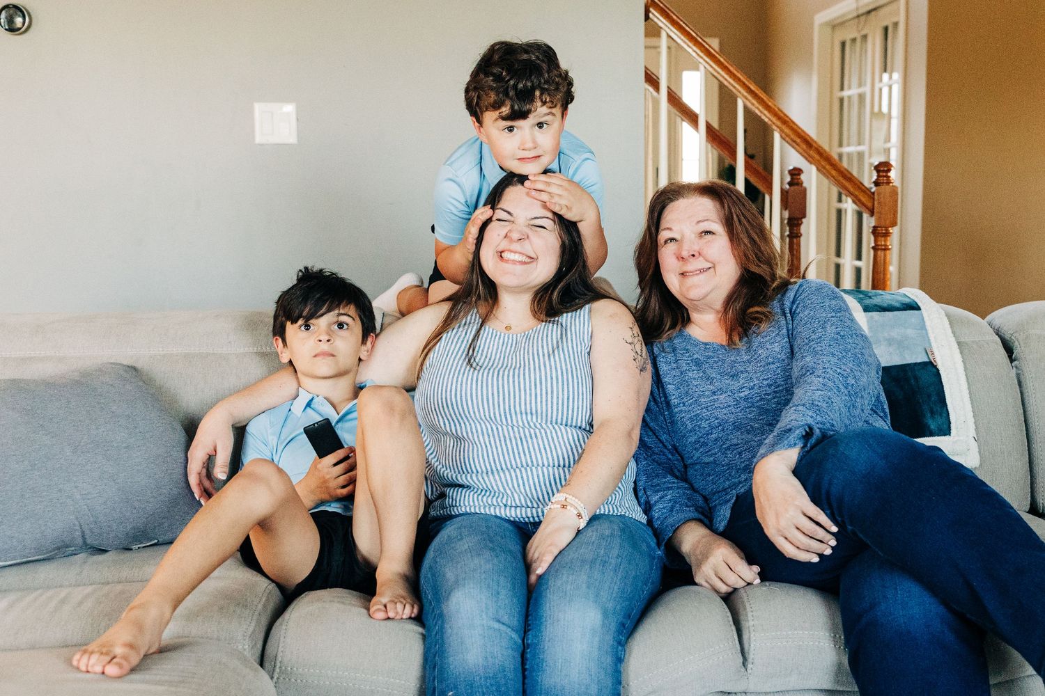 Happy family with two boys and two women smiling together on a cozy living room couch.