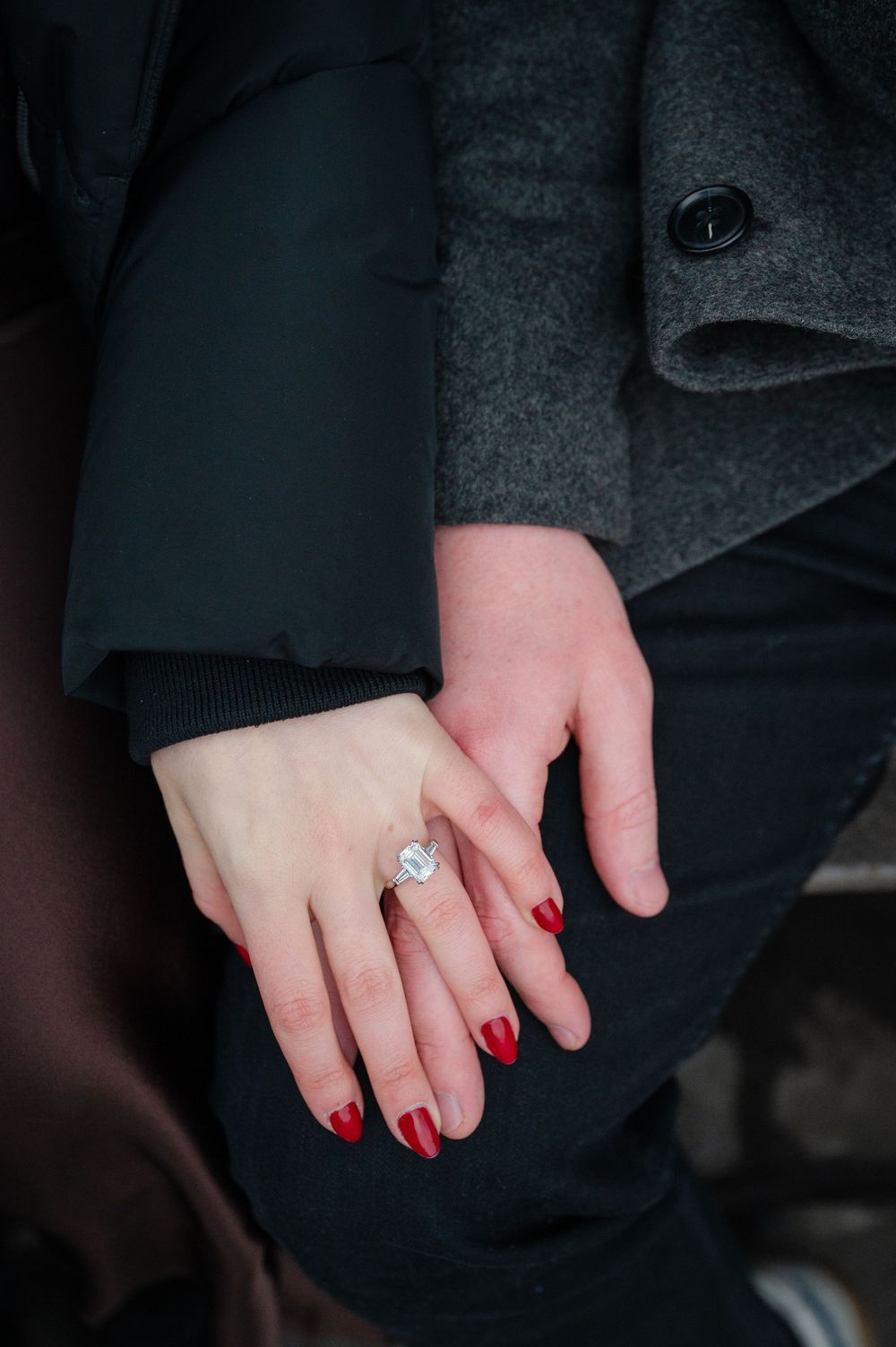 Close-up of an engagement ring with a large diamond on a woman's hand with red nails.