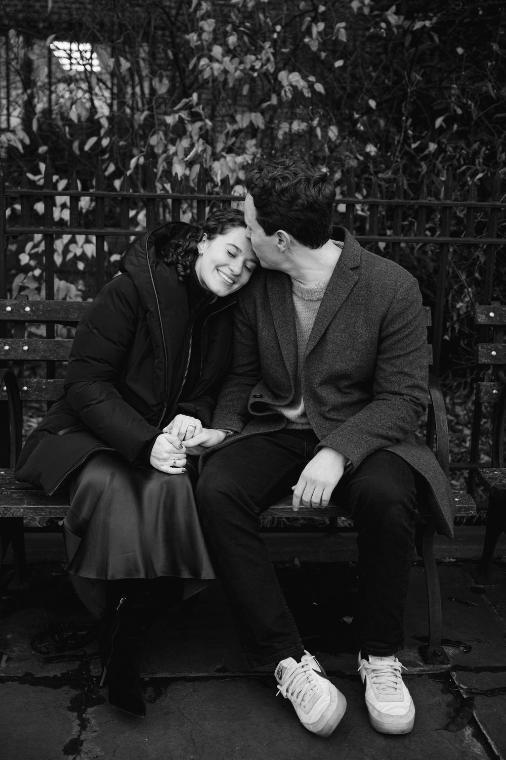 Couple sitting on a bench sharing a tender moment, black and white photo with lush garden backdrop.
